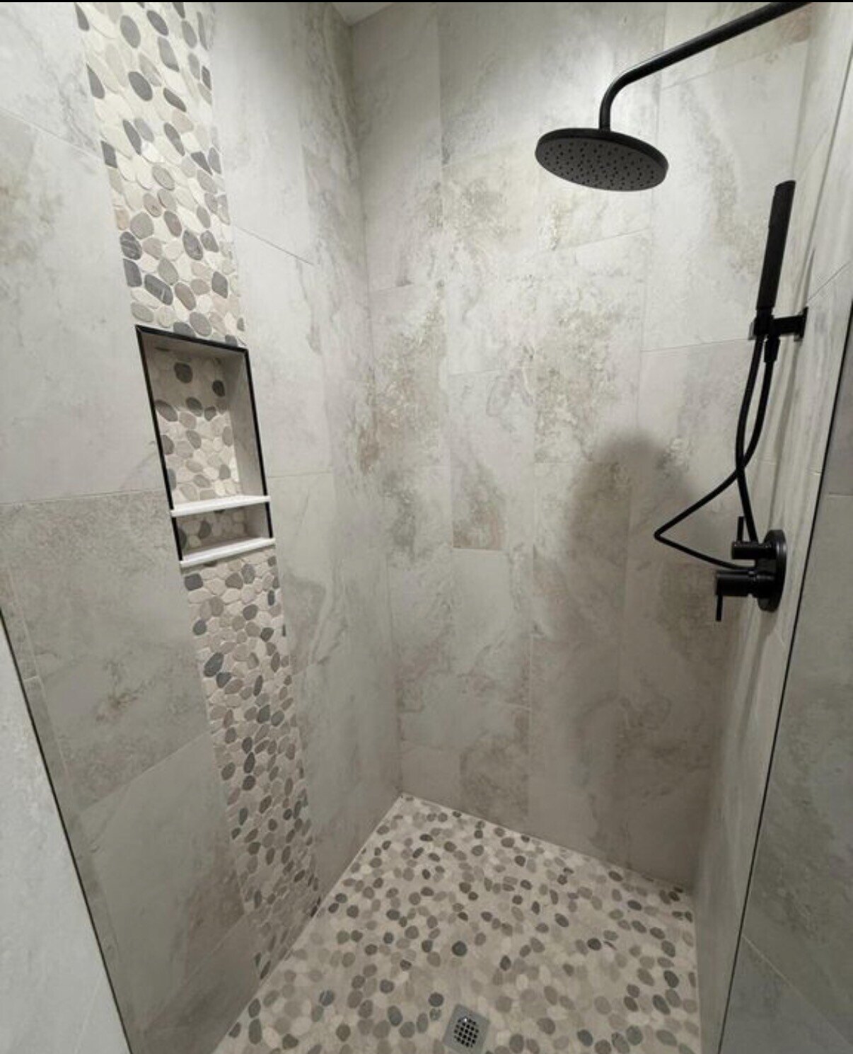 Finished custom tile shower with pebble accents and matte black fixtures